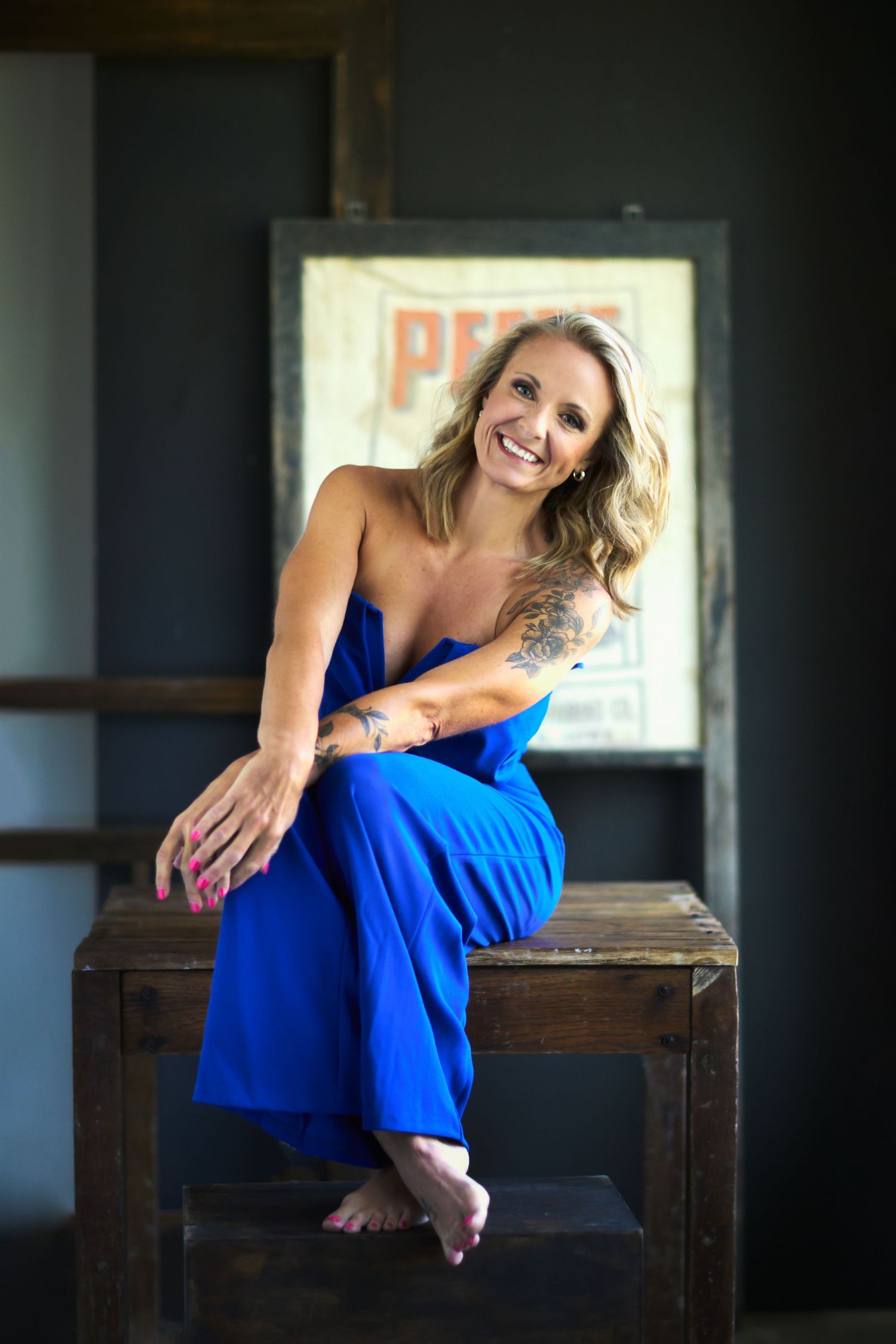 Vibrant portrait in blue dress sitting on wooden table with natural lighting.