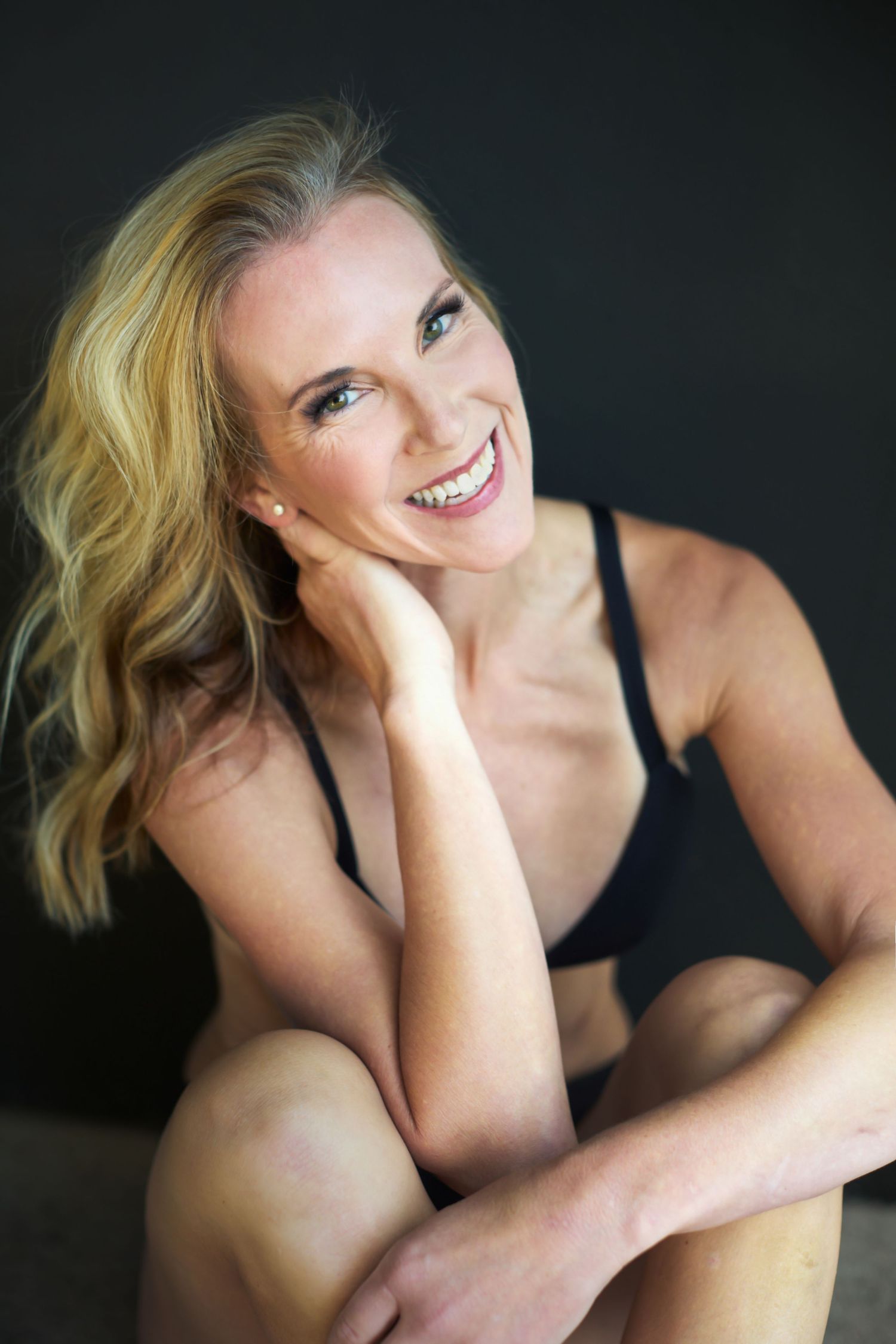 Intimate black and white portrait against dark background with natural smile.