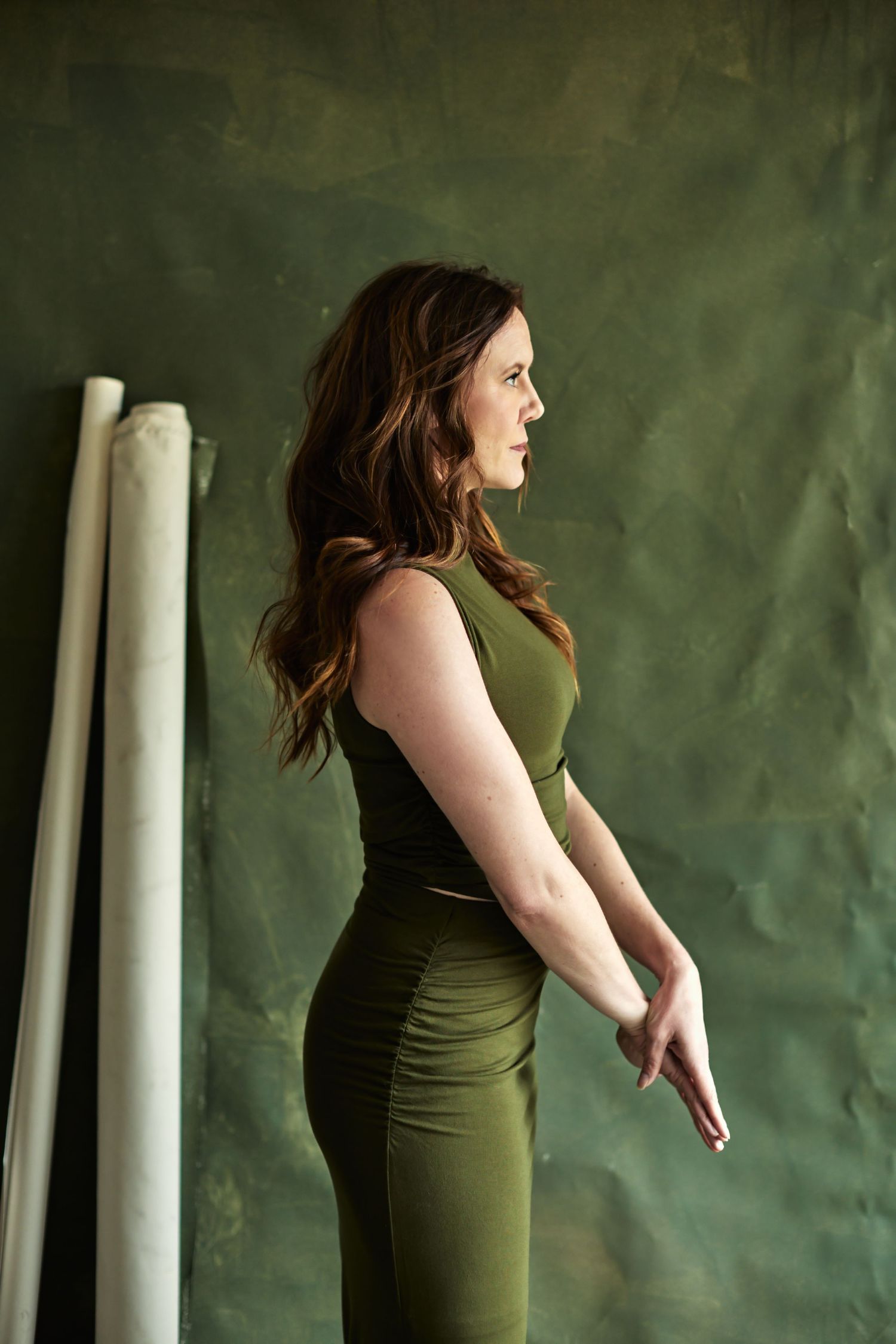 Elegant portrait in olive green dress against textured wall background.