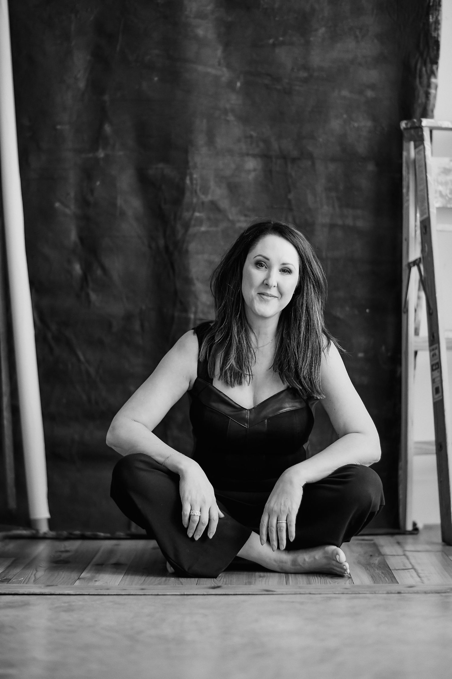 Black and white studio portrait in casual sitting pose against dark backdrop.