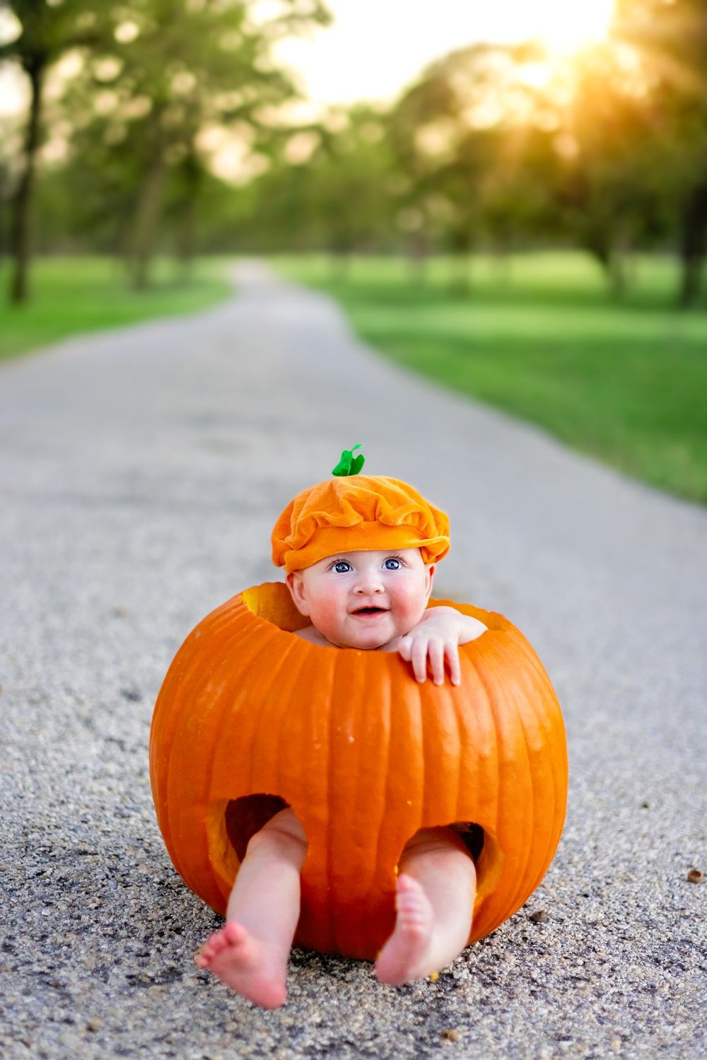 Baby sitting inside large orange pumpkin on gravel path.