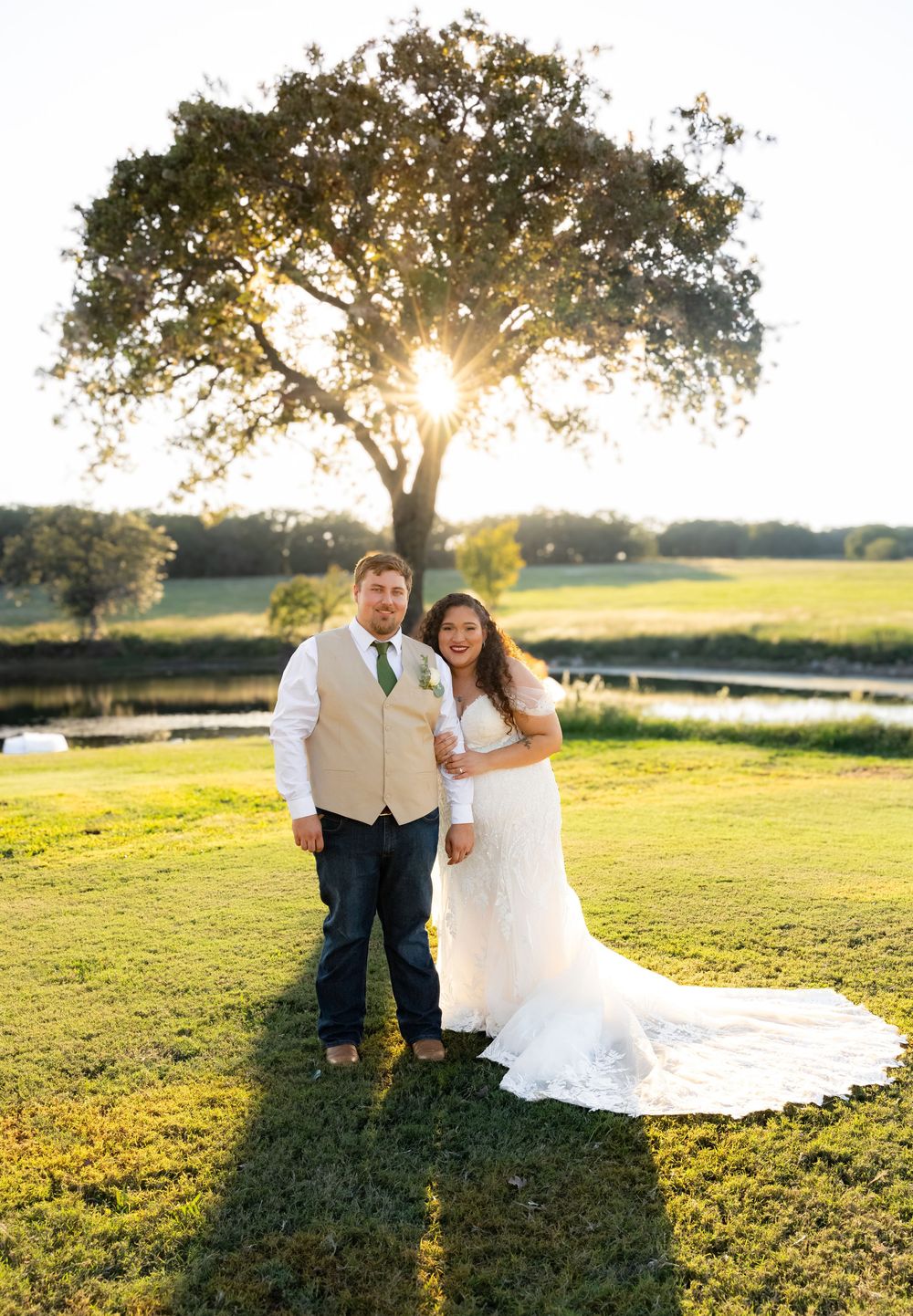 Couple in wedding attire sitting on grass during golden hour.