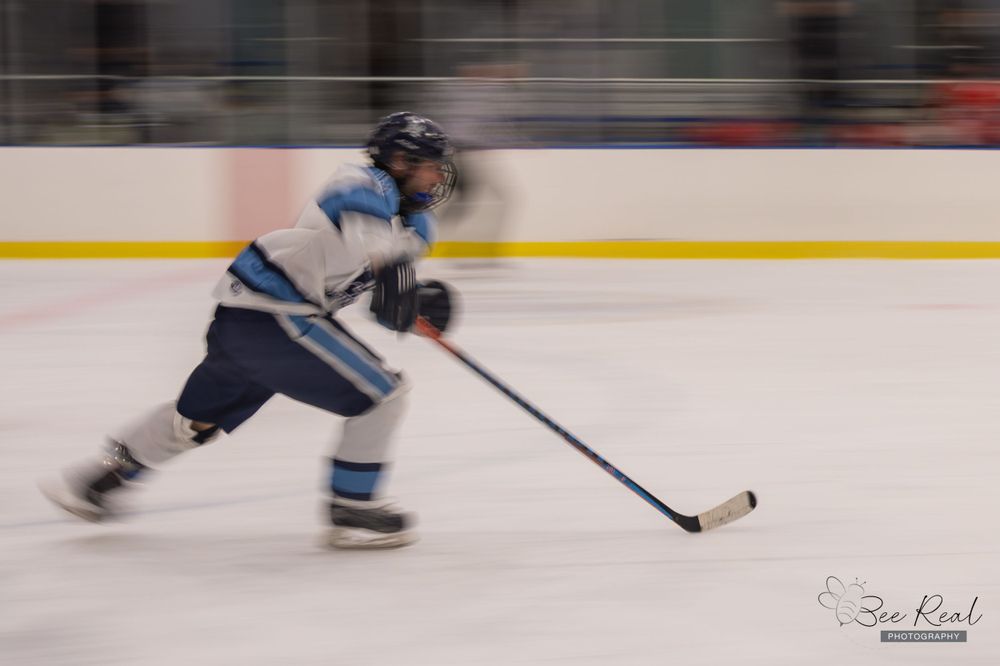 Hockey player in motion blur skating with puck on indoor ice rink.