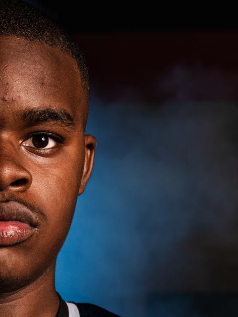 Close-up portrait with dramatic side lighting against blue background.