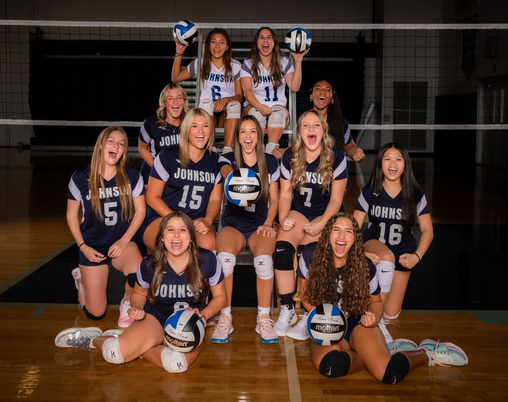 Volleyball team in navy uniforms poses together in indoor gymnasium.