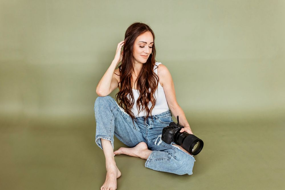 A photographer in casual denim sits cross-legged with a professional camera on a plain backdrop in New Haven, Connecticut