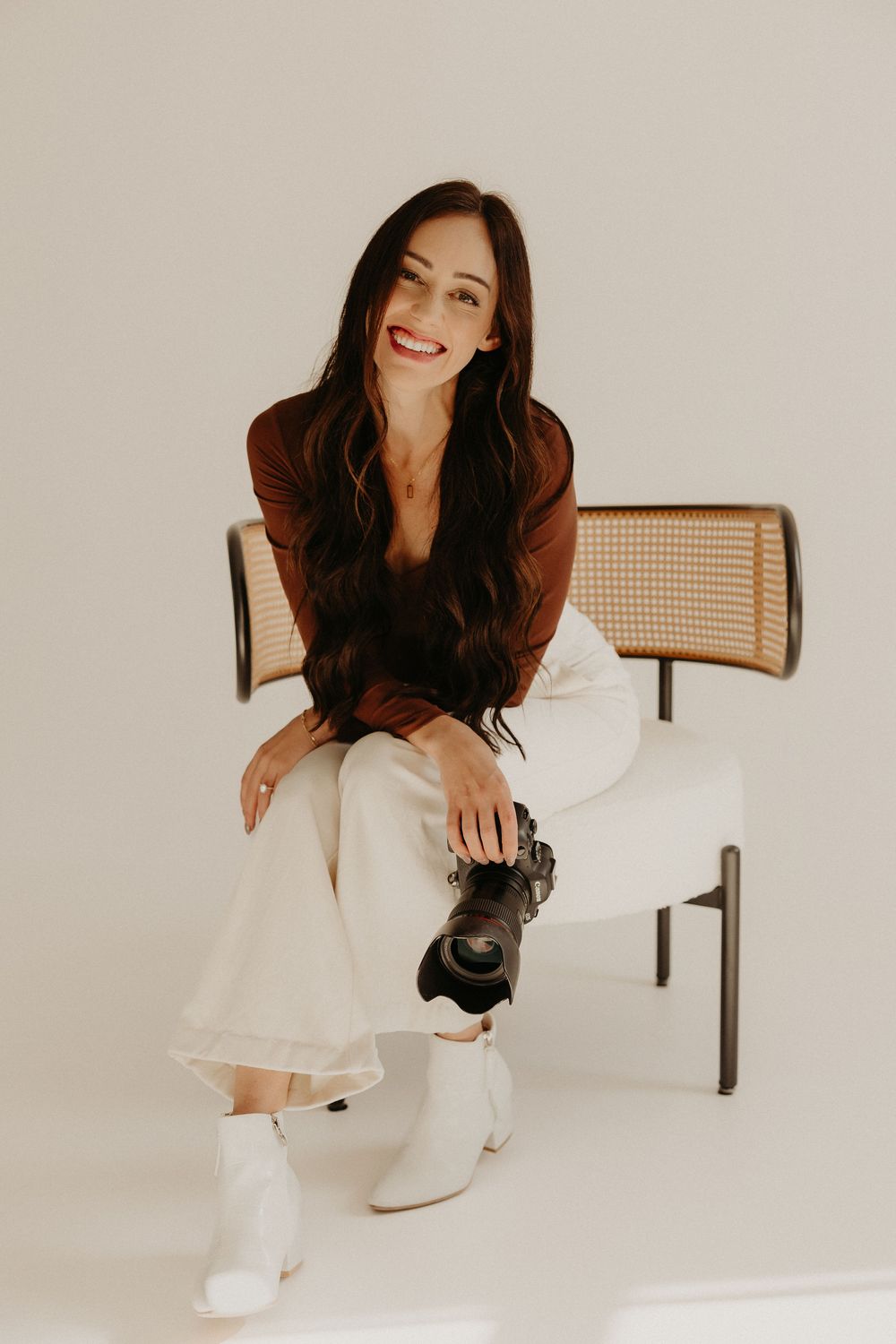 A person in a burgundy top and white pants sits on a cane chair wearing white boots against a light background in Waterbury, CT