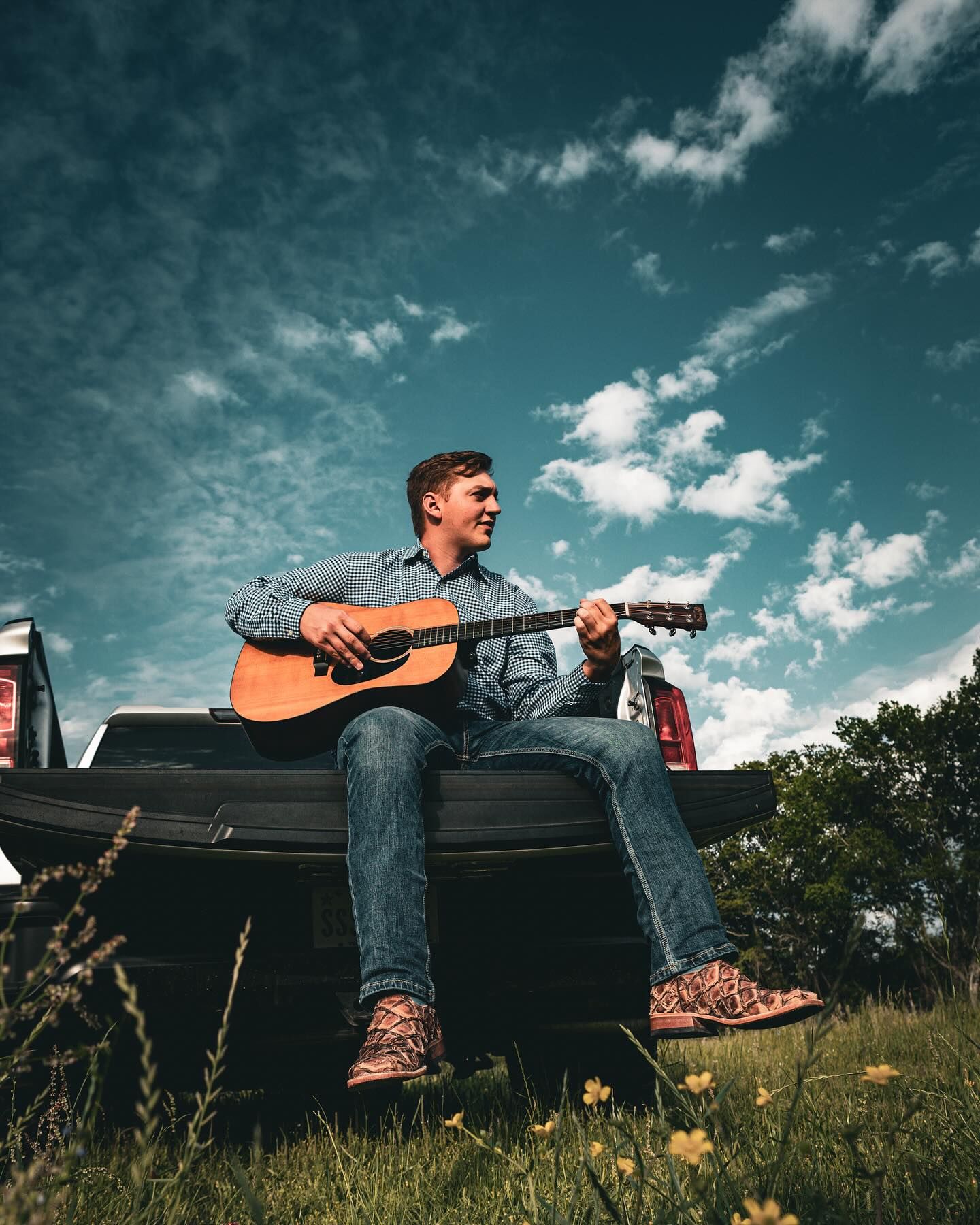 A person lying comfortably in a pickup truck bed parked in a grassy field under a dramatic blue summer sky.