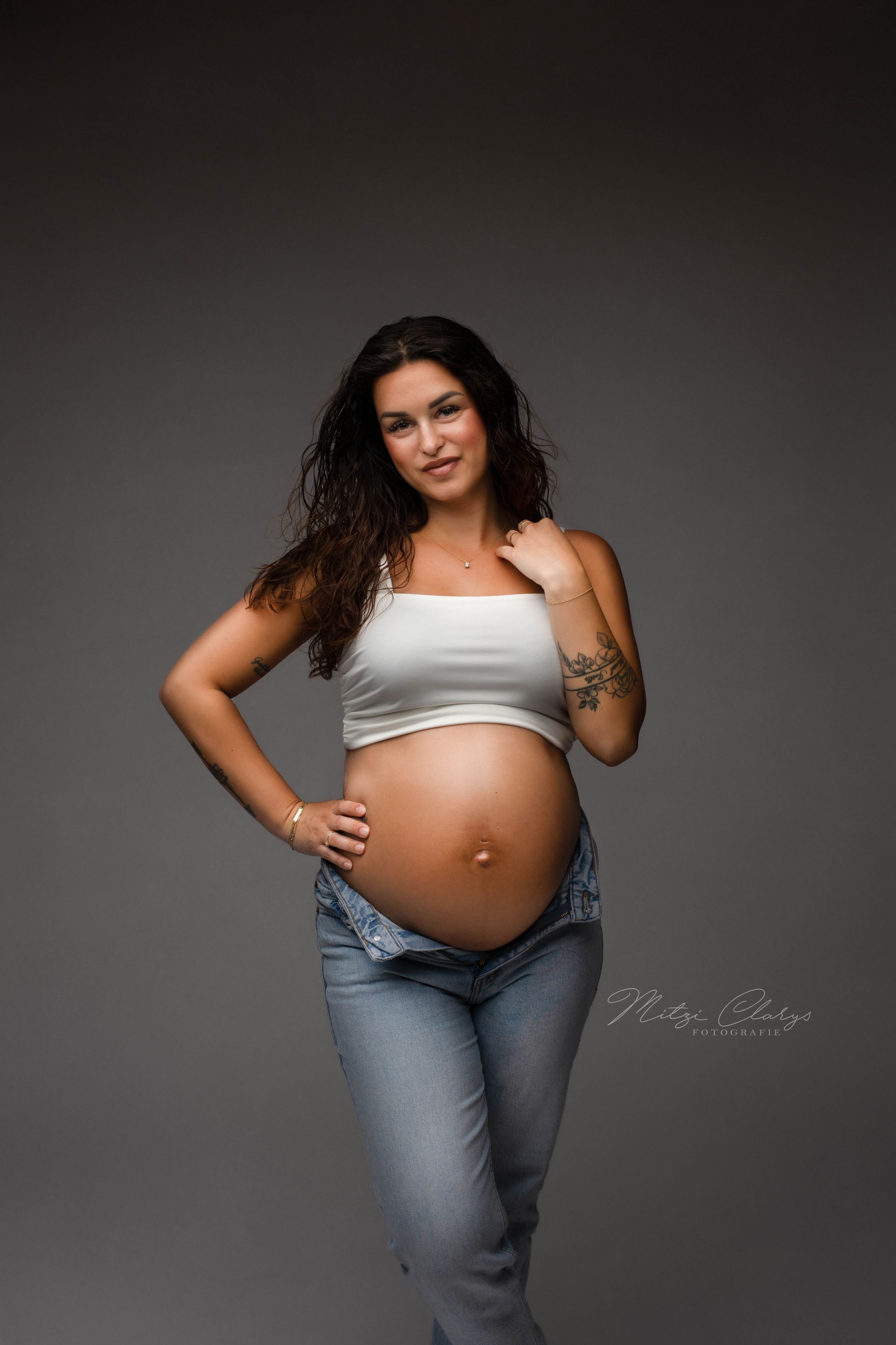 Tijdloos minimalistisch beeld van zwangere vrouw in spijkerbroek met witte top tijdens zwangerschaps fotoshoot