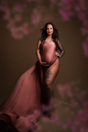 Zwangere vrouw met roze, zijden doek en bloemen tijdens zwangerschapsshoot