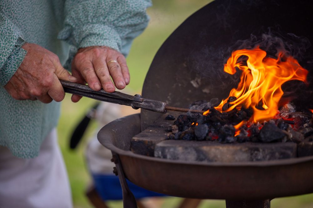 Person using metal tongs to tend a blazing fire in a cast iron grill with glowing hot coals.