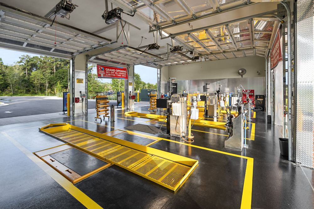 Modern vehicle inspection bay with yellow safety markings, lift ramps, and open garage doors in a clean facility.