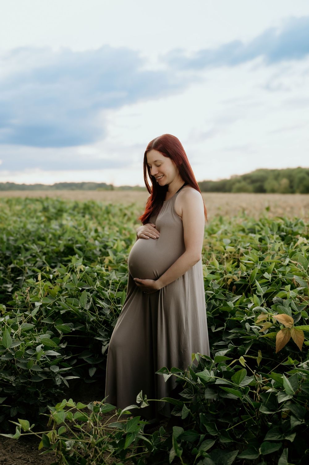 Maternity portraits in a verdant crop field under cloudy skies.