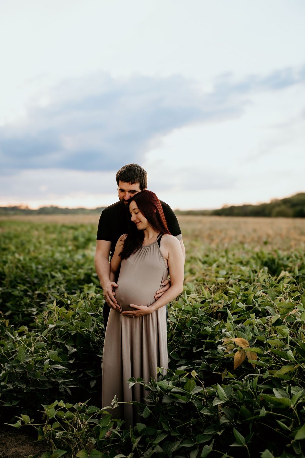 Intimate maternity photoshoot captured in a scenic agricultural field at dusk.