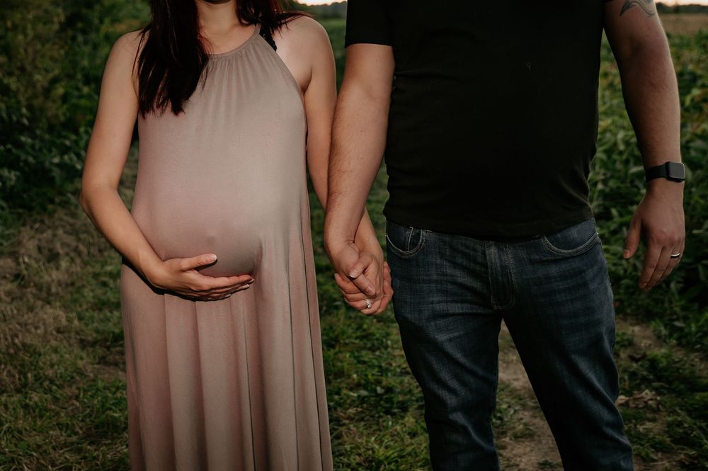 Expecting couple holding hands and embracing in casual outdoor maternity session.