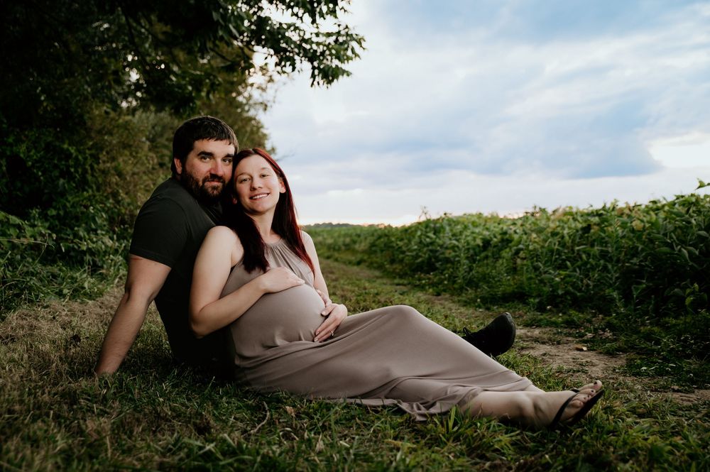 Couple relaxes together during outdoor maternity session in field.