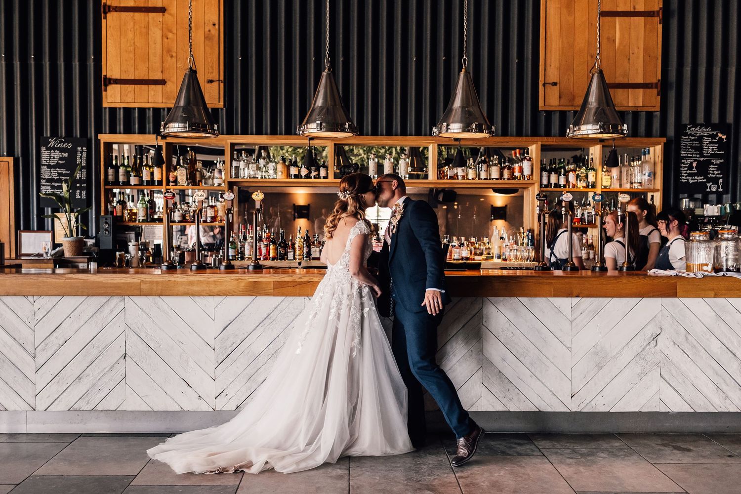 Bride and groom sharing a romantic moment at an elegant bar with pendant lights and a marble counter.
