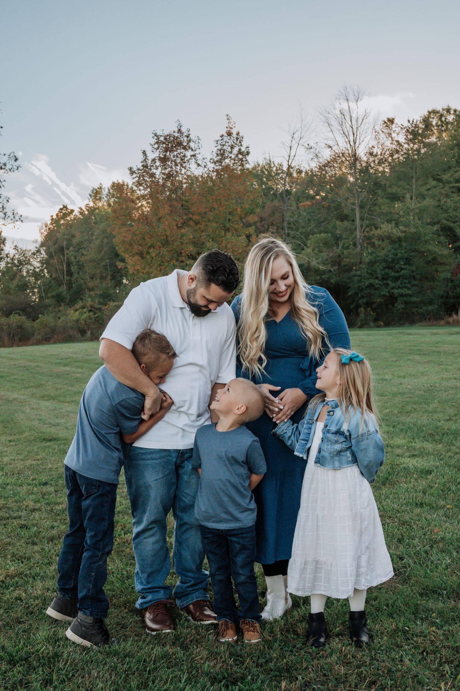 Pregnant mother and father celebrate with three children in an open field during a maternity photo session.