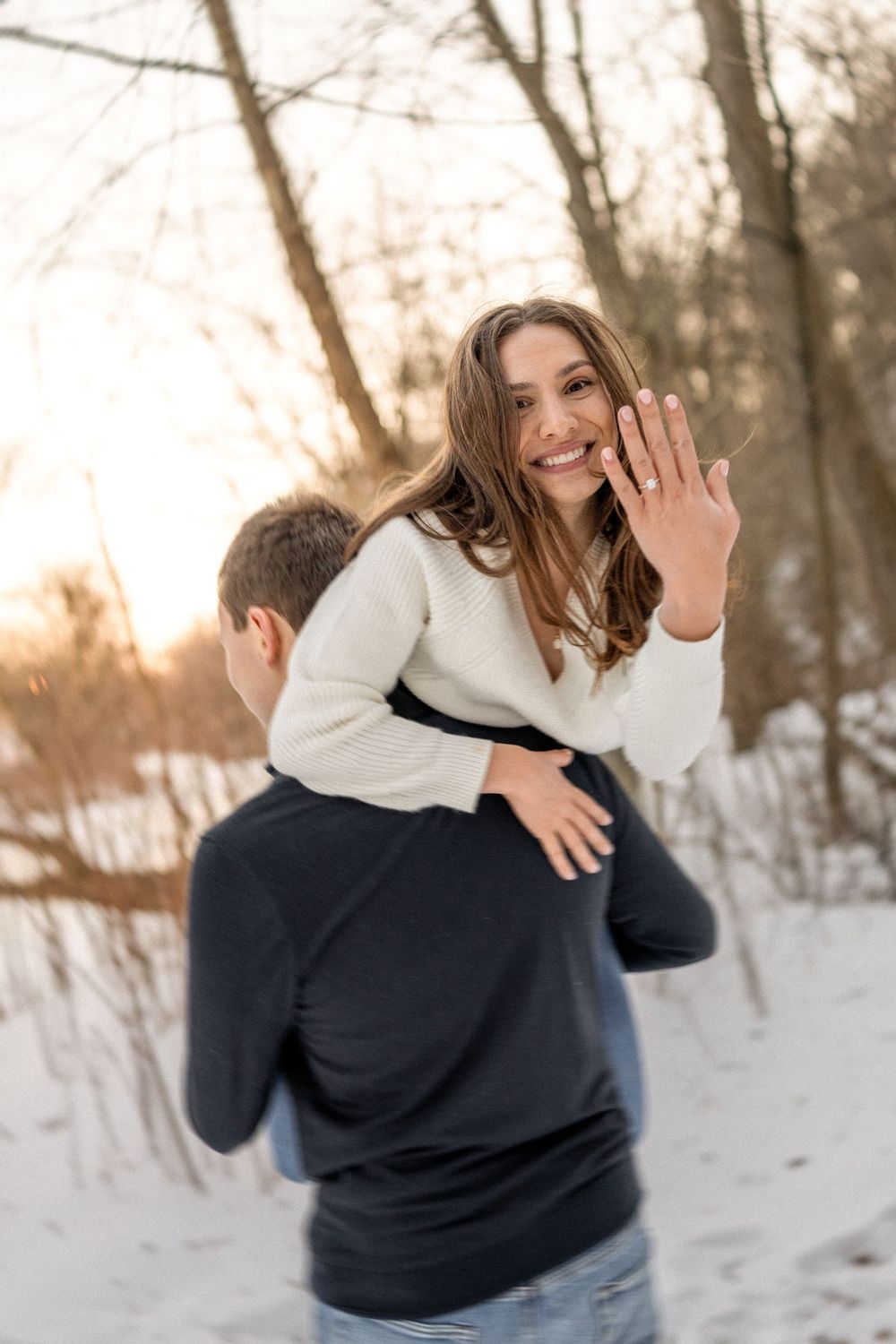 A person in a navy and white sweater plays in the snow during a winter photoshoot at sunset.