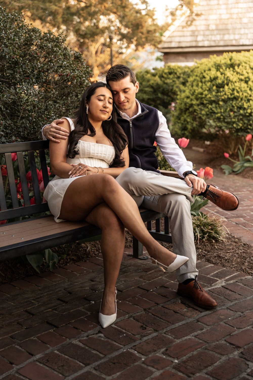 Romantic couple sitting together on a rustic garden bench at sunset on brick patio.