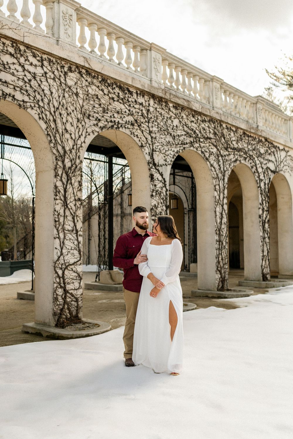 A couple shares romantic moments under a beautiful arched colonnade with climbing vines and white architecture.