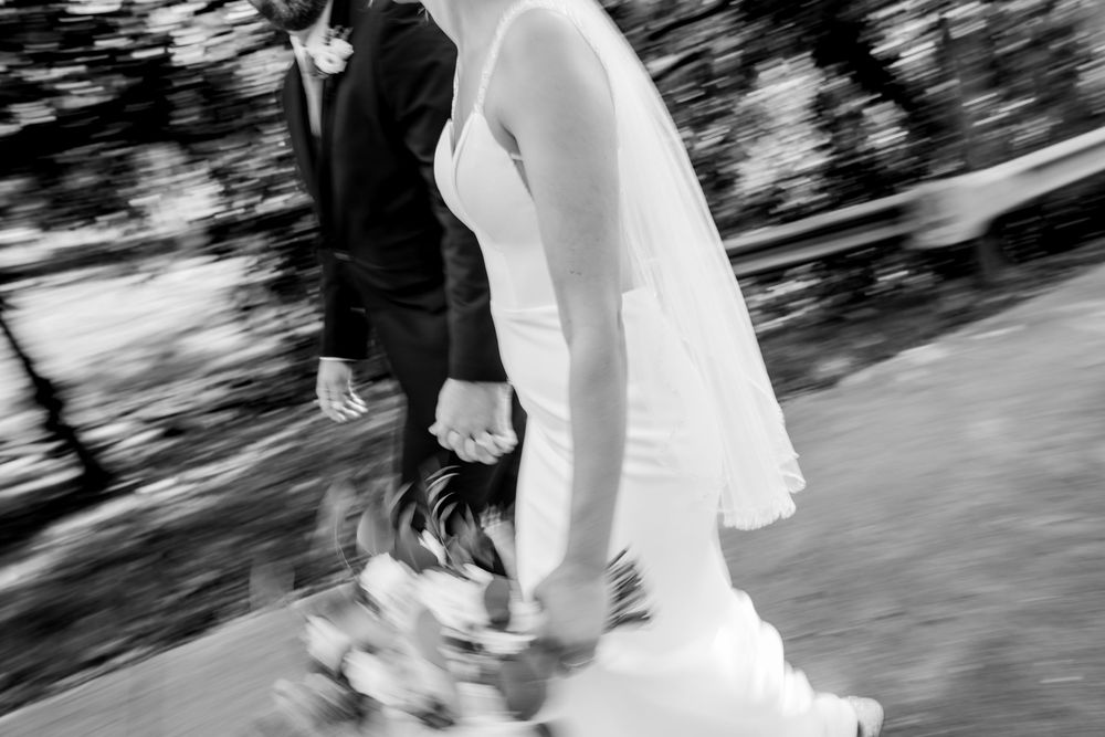 Black and white photo of bride and groom walking hand in hand, motion blur capturing wedding day elegance.