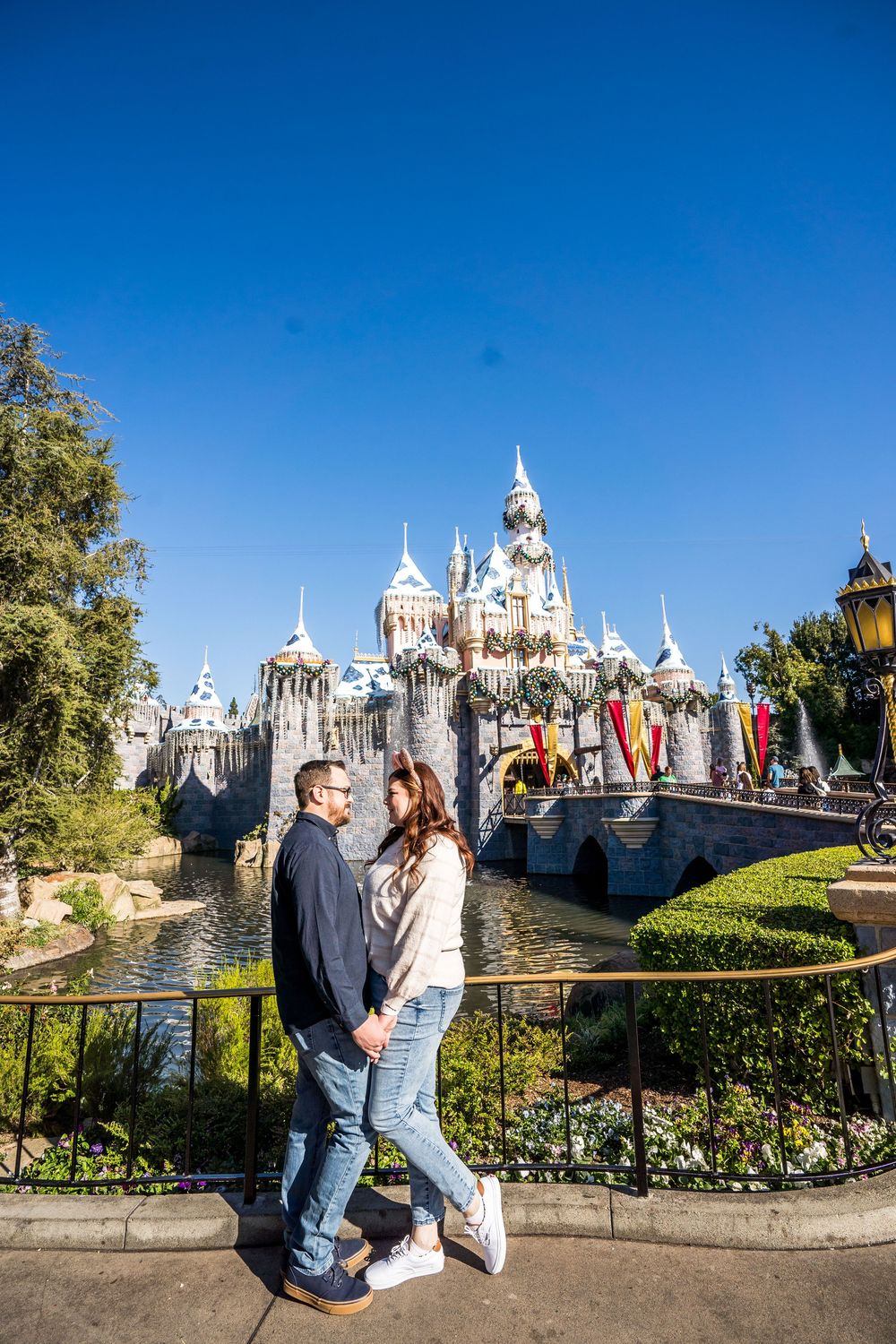 Couple holding hands in front of Sleeping Beauty Castle at Disneyland on a sunny day.