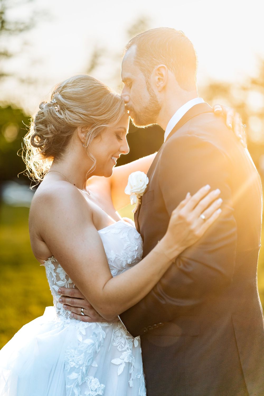 Bride and groom embracing at golden hour sunset, sharing a romantic moment in wedding attire outdoors.