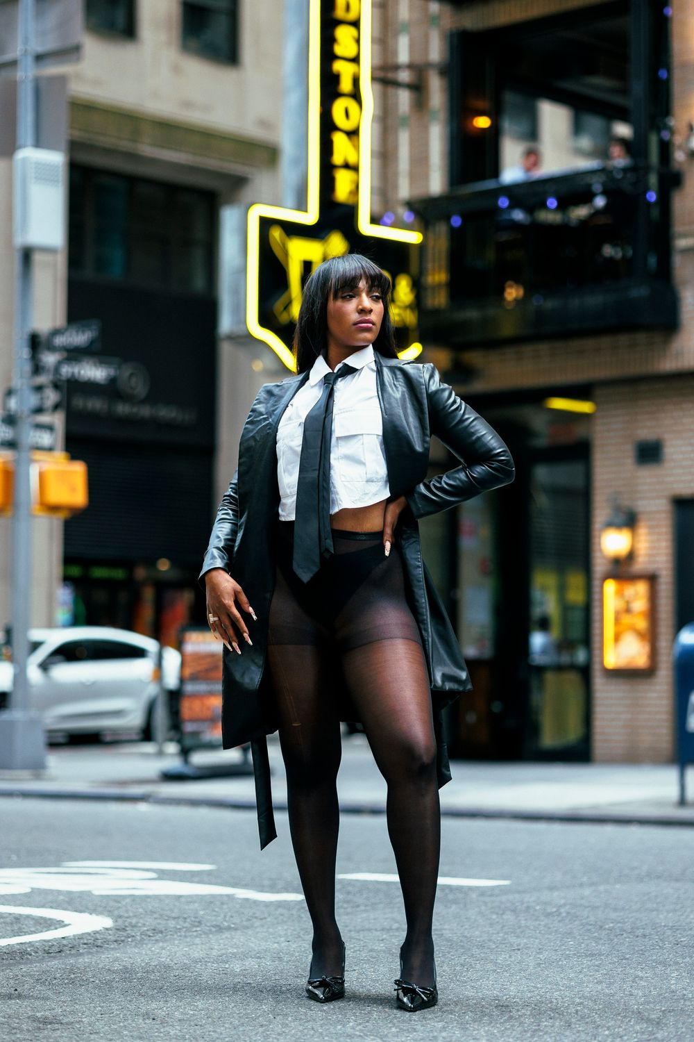 Close-up of black leather boots and tights on city street with neon signs in background.