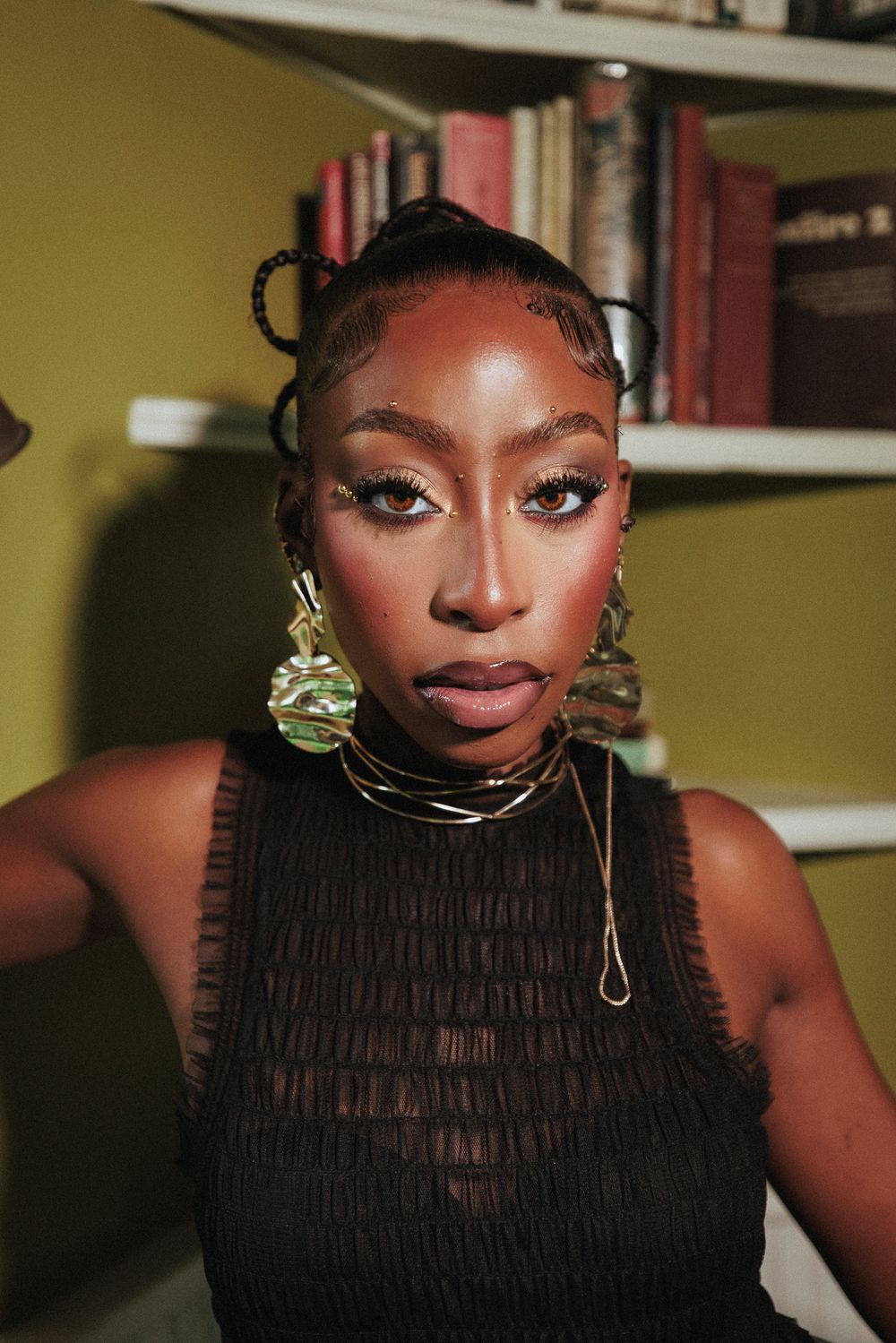 Close-up portrait with dramatic makeup and black textured top in warm lighting.