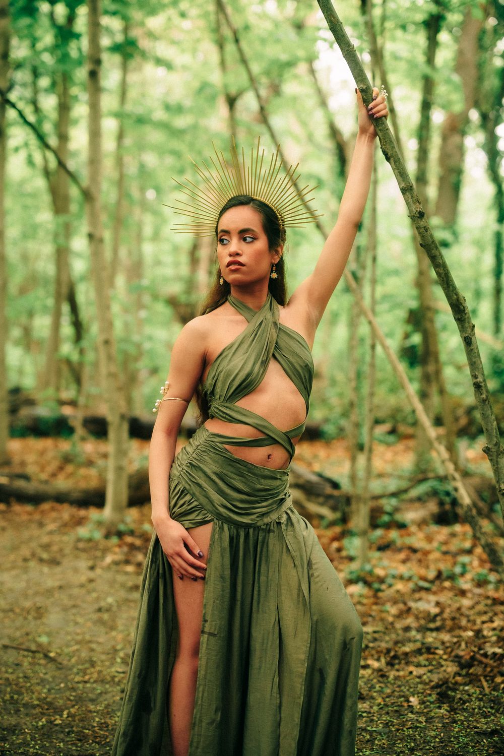 Artistic forest photoshoot featuring olive green flowing dress among trees.