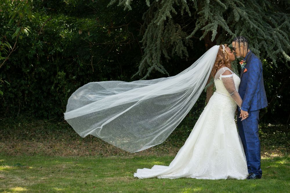 Newlyweds kissing outdoors with flowing veil in garden setting.
