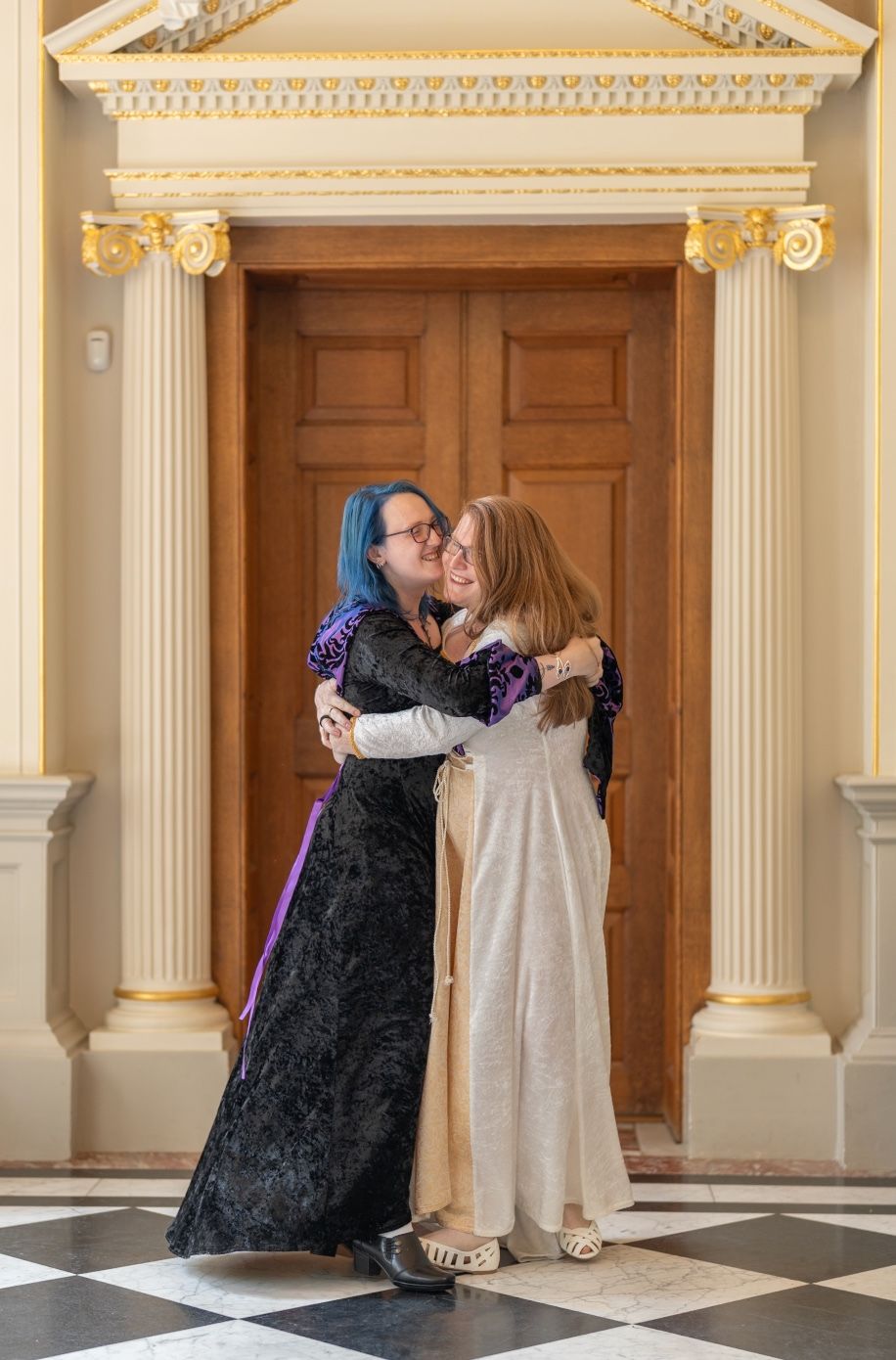 Couple embracing in wedding attire beneath ornate classical doorway.