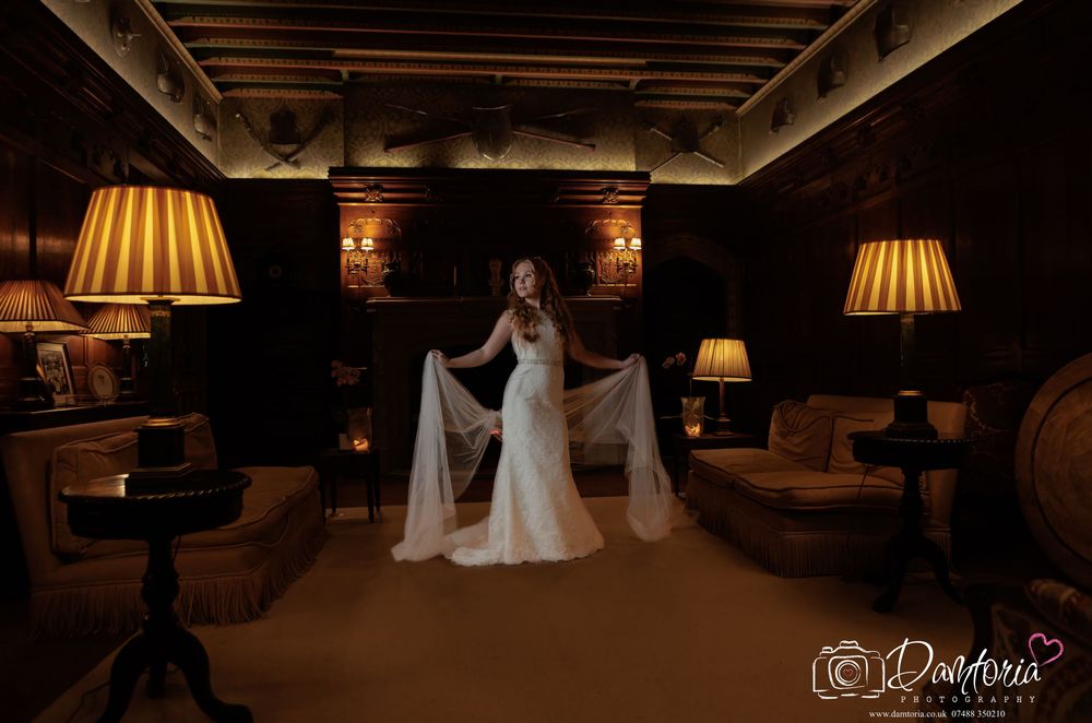 Bride in elegant white gown poses in dimly lit rustic venue with warm lamp lighting creating dramatic ambiance.