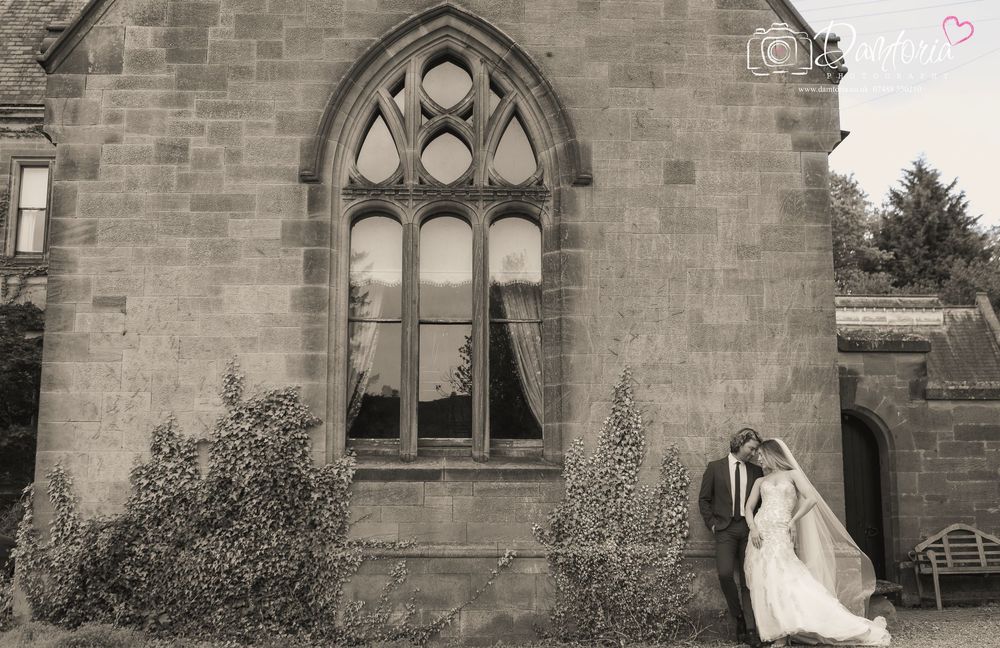 Bride and groom share a romantic kiss outside a Gothic stone chapel with arched windows on their wedding day.