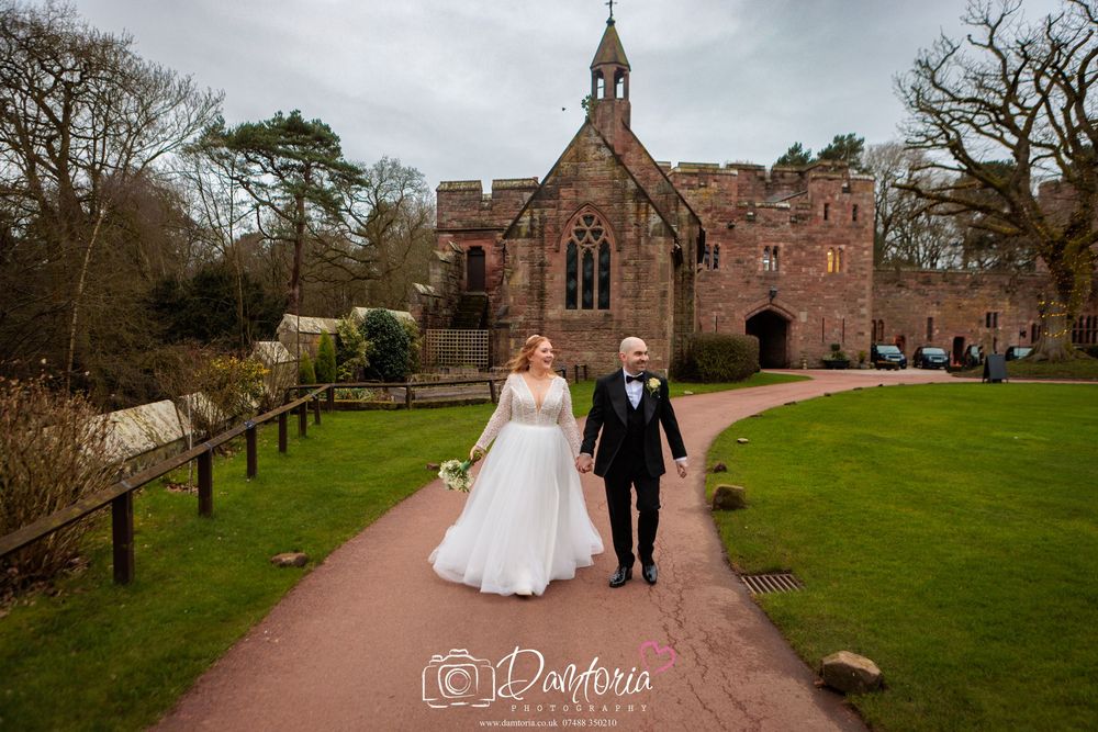 A couple walks down a path in front of a historic stone church with Gothic architecture on their wedding day.