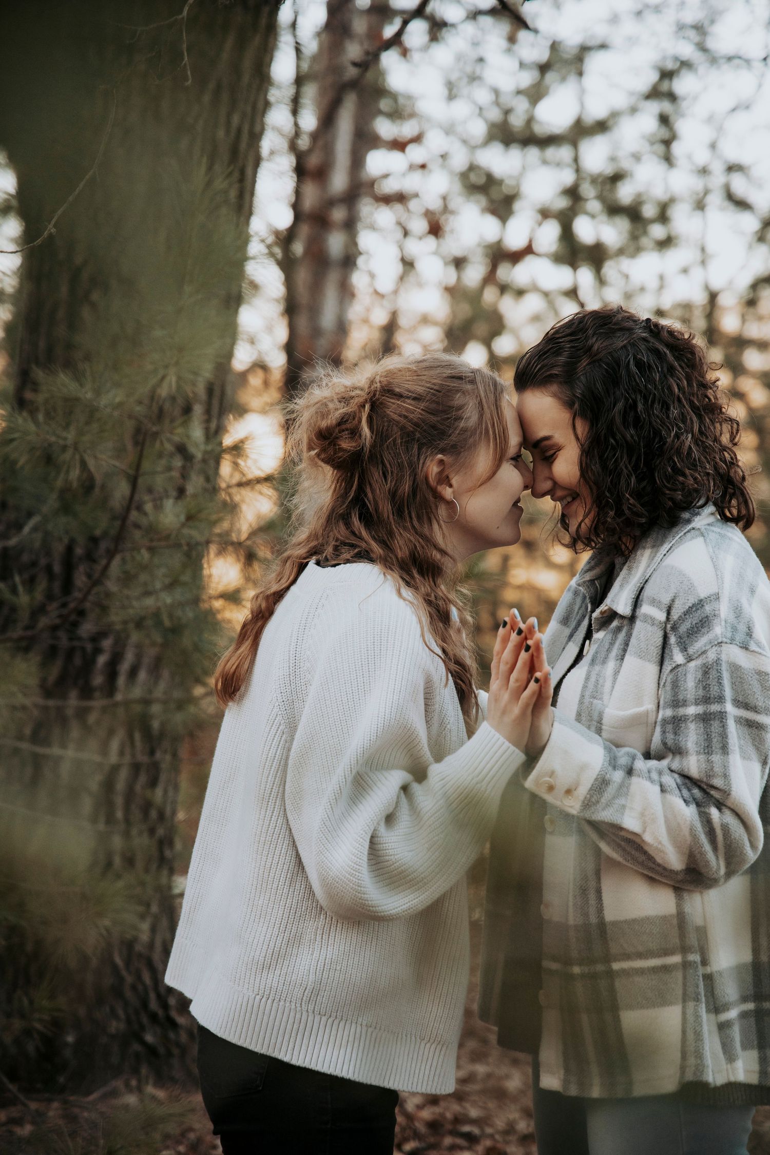 Two people share an intimate moment in a forest setting wearing cozy sweaters at sunset.