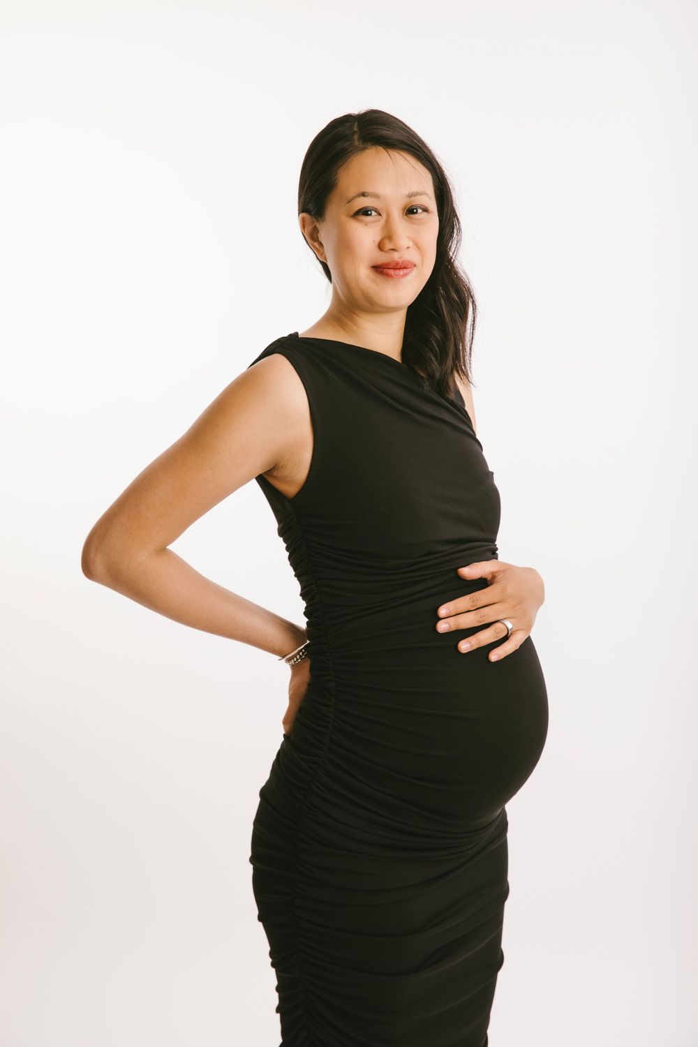A pregnant woman in a black dress poses against a white backdrop showing her growing belly from different angles.