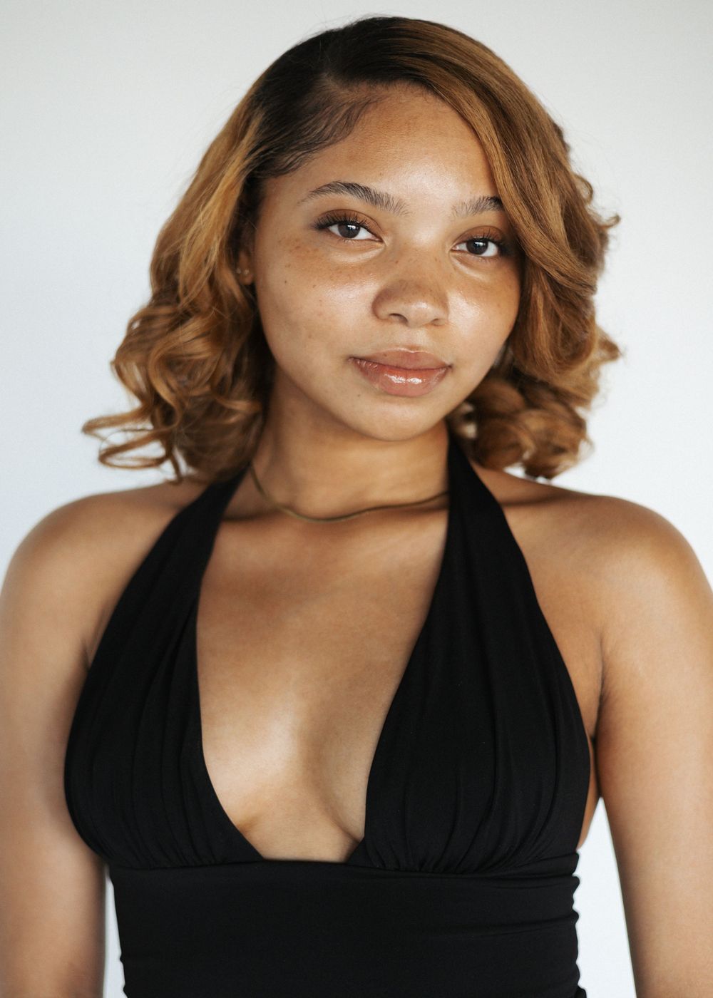 Woman with curly brown hair wearing black halter top poses in headshot series against white background.