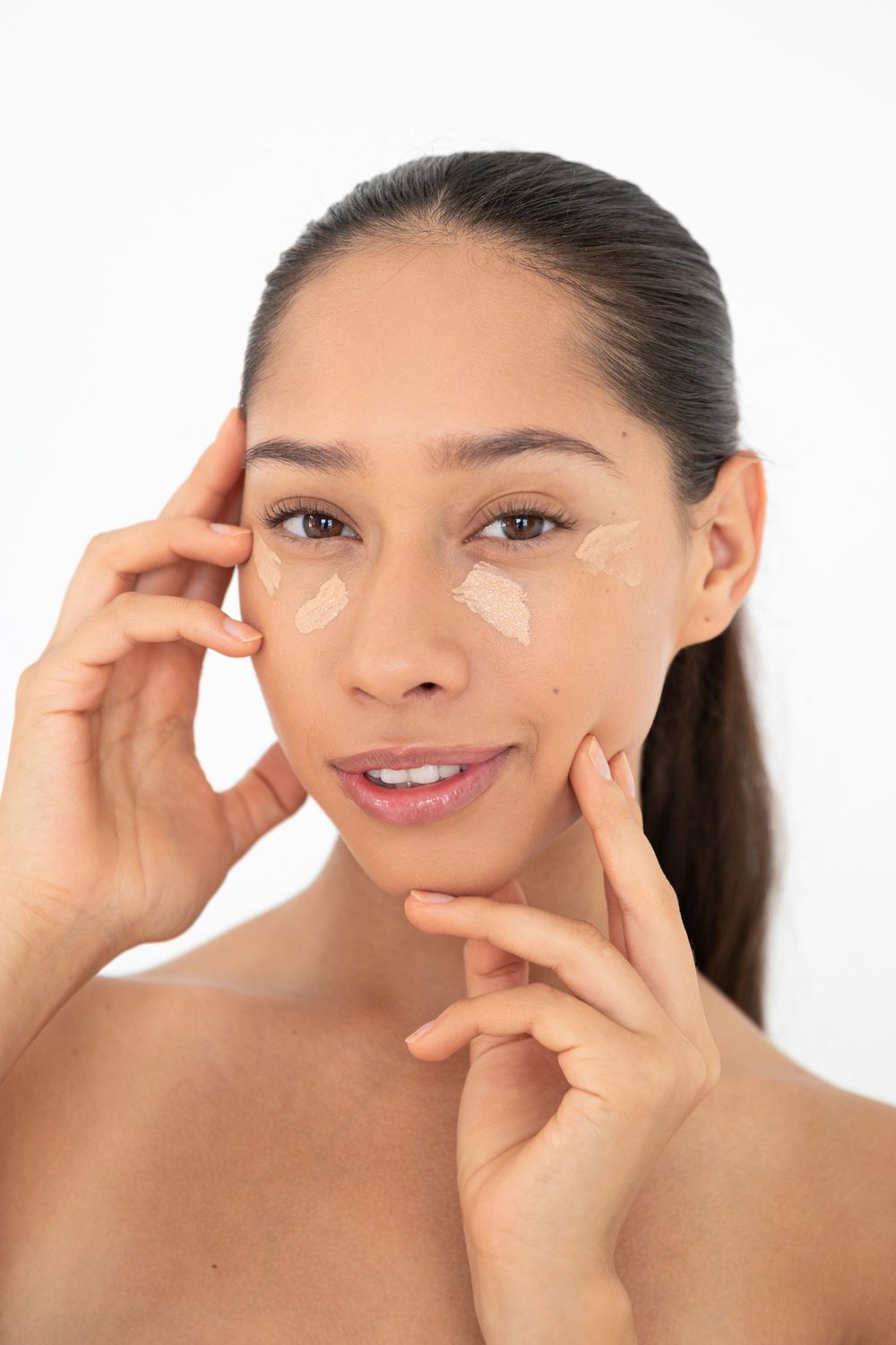 Woman applying eye cream moisturizer to under-eye area, skincare beauty routine on white background.