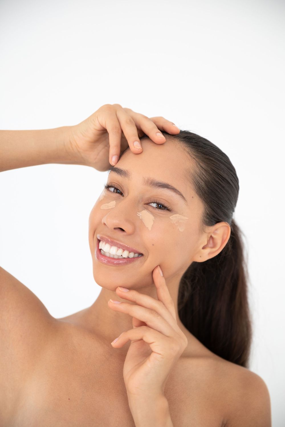 Smiling woman applying moisturizer cream to her face against a white background for skincare routine.