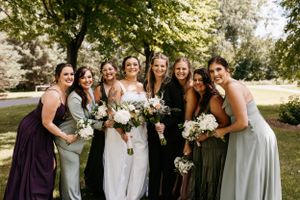 Wedding party with bridesmaids in mix-matched dresses poses together holding white floral bouquets in an outdoor garden setting.