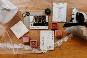 Wedding invitation suite with stationery, rings, and decorative elements laid out on wooden surface.