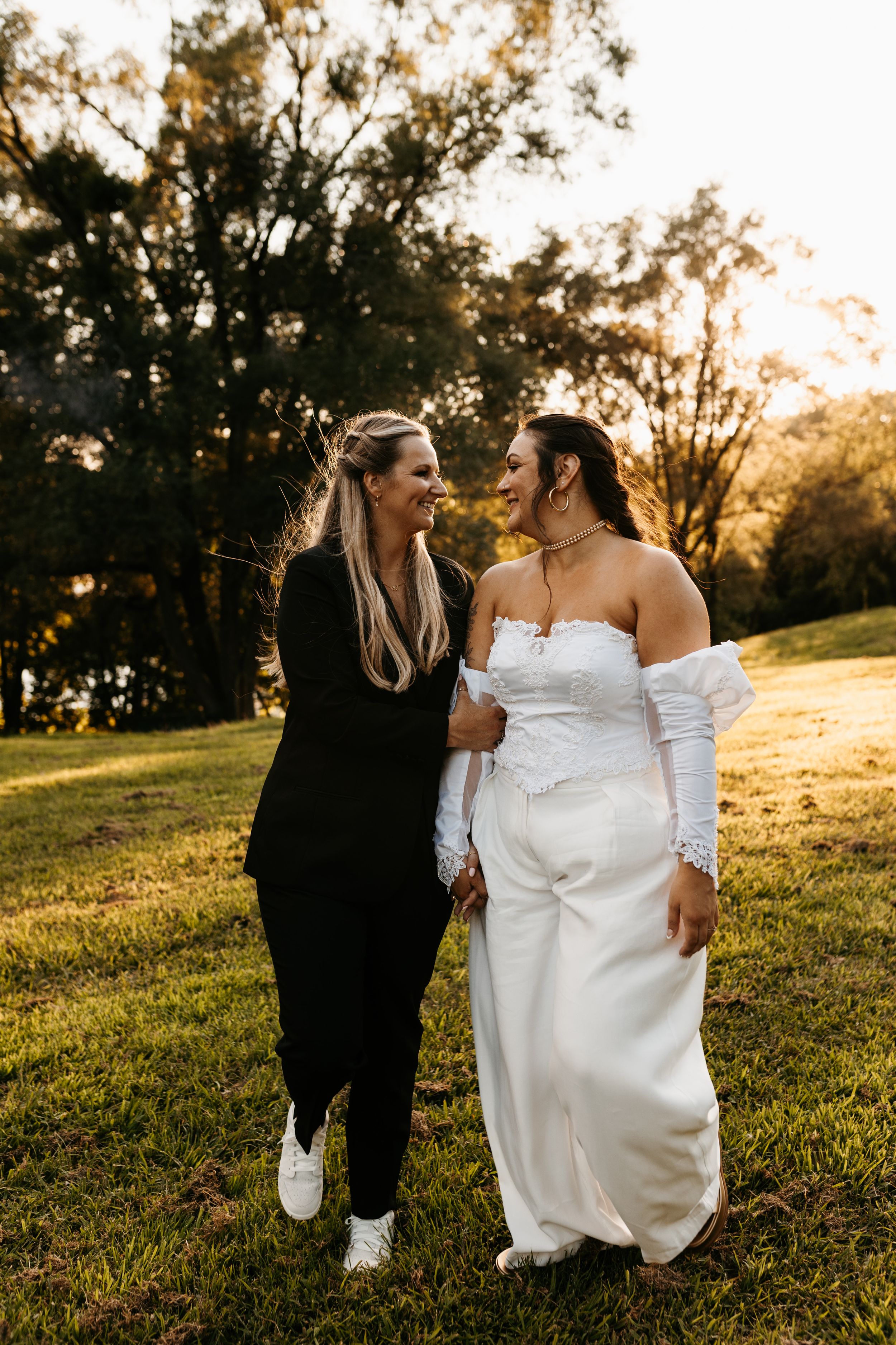 Two people sharing a candid moment while walking on grass during golden hour sunset.