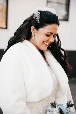 Winter bride wearing elegant white fur wrap and crystal hair accessory smiles with bouquet.