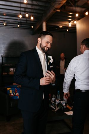 Wedding guest in dark suit enjoying reception under industrial-style string lights.
