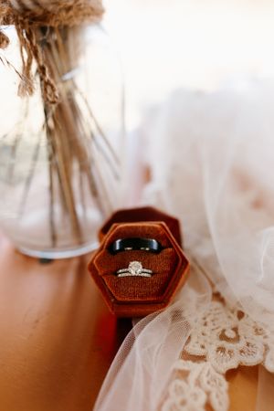 An engagement ring sits in a velvet hexagonal box with lace veil details.