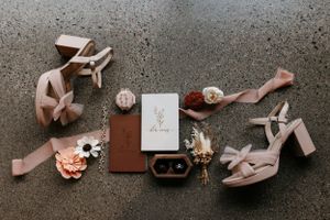 Wedding details flat lay with pink shoes, jewelry, and stationery on concrete background.
