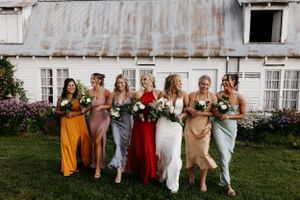 Bridesmaids in mix-matched dresses walking together in front of a rustic white building.
