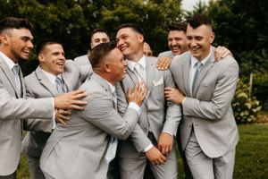 Groomsmen in light gray suits sharing a playful moment outdoors.